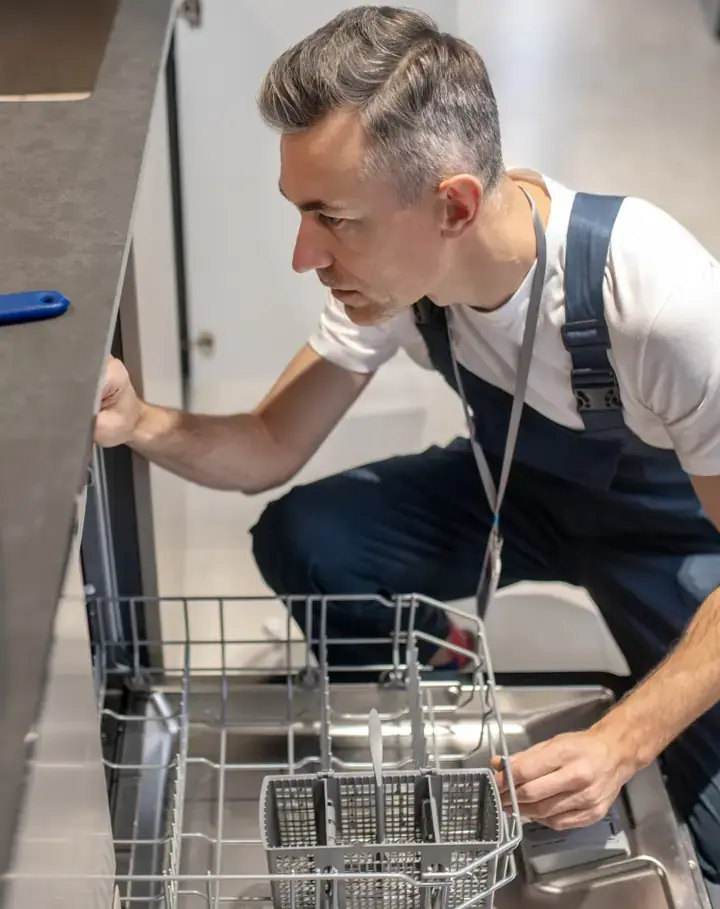 Appliance repair technician checking a dishwasher in a customer's kitchen
